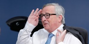 Ο Ζαν Κλοντ Γιούνκερ με το σακάκι του ριγμένο στον ώμο, χαιρετάει