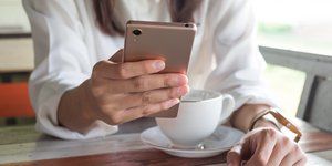 Γυναίκα κρατά κινητό και πίνει καφέ