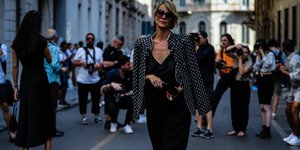 Ξανθιά γυναίκα με μαύρη ολόσωμη φόρμα, σακάκι και γυαλιά 