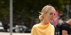 Μια γυναίκα με κίτρινη πλεκτή μπλούζα και καφέ παντελόνι στο δρόμο