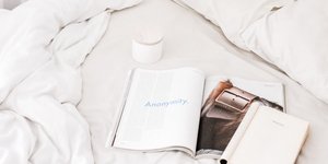 Γυναικεία κρεβατοκάμαρα με λευκά κλινοσκεπάσματα, περιοδικά, βιβλία και μια κούπα