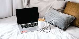 Γυναικεία κρεβατοκάμαρα με γκρι και καφέ μαξιλάρια, λάπτοπ, κούπα με καφέ
