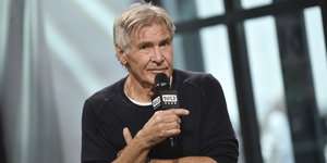 Ο Χάρισον Φορντ κρατάει μικρόφωνο και φοράει μαύρη μπλούζα 