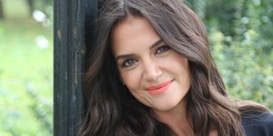 Η Κέιτι Χολμς ακουμπά σε κολόνα και χαμογελά στην κάμερα