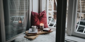 Κούπα, αναμμένο κερί και κόκκινο μαξιλάρι στο παράθυρο