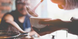 Χέρια κρατούν ένα μπολ με σούπα και βάζουν σούπα από την κατσαρόλα
