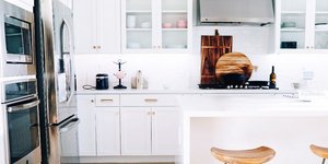 Κουζίνα με λευκά έπιπλα, ξύλινα σκαμπό, ψυγείο 