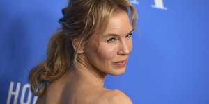 Η Ρενέ Ζελβέγκερ με πιασμένα τα μαλλιά και μπλε φόντο 