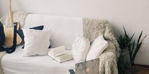 Σαλόνι διαμερίσματος με λευκό καναπέ, κρεμ χαλί, πουφ, κιθάρα, ένα φυτό, βιβλία