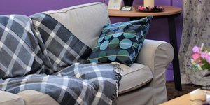 Γκρι καναπές, ξύλινο τραπέζι, μωβ τοίχος, βάζα με λουλούδια 