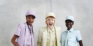 Τρεις γυναίκες με μωβ, κίτρινο, γαλάζιο κοστούμι χαμογελούν στον φακό