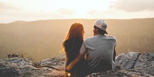 Ενα ζευγάρι κάθεται σε βράχια και απολαμβάνει τη θέα, ο άνδρας φοράει καπέλο