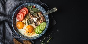 Αυγά, ντομάτες, αγγούρι και πιρούνι σε ένα τηγάνι και δίπλα φέτες ψωμιού