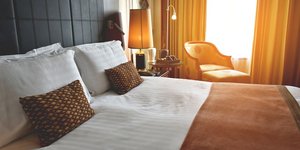 Κρεβάτι σε δωμάτιο ξενοδοχείου με δύο μαξιλάρια, κουρτίνα, πολυθρόνα, κομοδίνο