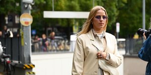 Γυναίκα περπατάει με μπεζ παλτό και γυαλιά