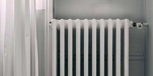 Λευκό καλοριφέρ δίπλα σε λευκή κουρτίνα και ξύλινο πάτωμα
