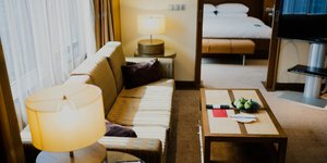 Σαλόνι με καναπέ, λάμπα στο πλάι και στο βάθος φαίνεται το κρεβάτι 