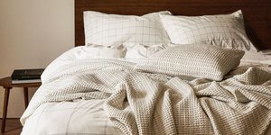 Ενα ξύλινο κρεβάτι με λευκά σεντόνια και ριχτάρι