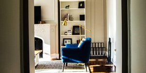 Καθιστικό διαμερίσματος με μπλε πολυθρόνα, μεταλλικό φωτιστικό, χαλί, βιβλιοθήκη