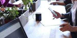 Υπάλληλοι κάθονται σε ένα μεγάλο τραπέζι και κοιτούν υπολογιστή και κινητό