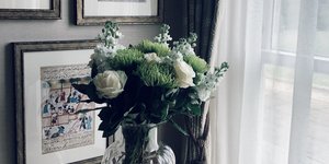 Ενα γυάλινο βάζο με λευκά τριαντάφυλλα πάνω σε τραπεζάκι δίπλα στο παράθυρο