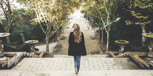 Γυναίκα με τζιν και μαύρο παλτό περπατάει στο δρόμο με την πλάτη της