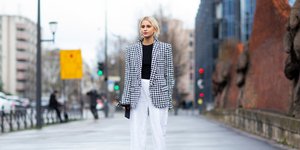 Γυναίκα με καρό σακάκι και λευκό παντελόνι στο δρόμο τον χειμώνα 