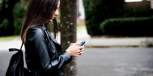 Γυναίκα με δερμάτινο μπουφάν κοιτάζει το κινητό της