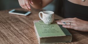 Βιβλίο, κινητό και κούπα καφέ γυναίκας σε τραπέζι