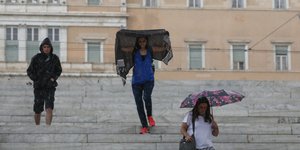 Περαστική καλύπτουν τα κεφάλια τους από την βροχή έξω από τη Βουλή