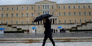 Γυναίκα περπατά με ομπρέλα μπροστά από τη Βουλή