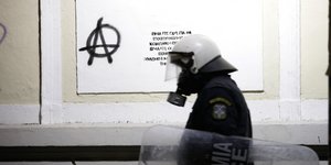 Αστυνομικός περπατάει, στο βάθος σύνθημα αντιεξουσιαστών