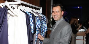 Ο Αγγελος Μπράτης με γκρι κοστούμι δίπλα σε ρούχα