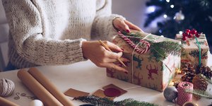 Γυναίκα με πουλόβερ τυλίγει ένα χριστουγεννιάτικο δώρο