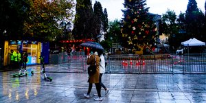 Γυναίκες περπατούν μπροστά από χριστουγεννιάτικο δέντρο στο Σύνταγμα με ομπρέλα