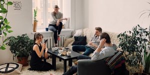 Μια παρέα τεσσάρων ατόμων κάθονται στο σαλόνι και μιλάνε γύρω από ένα τραπέζι