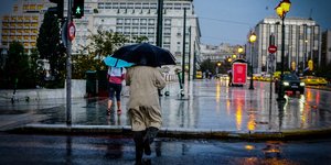 Ανδρας περνάει διάβαση κρατώντας ομπρέλα στο κέντρο της Αθήνας