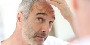 Άνδρας κοιτά τα λευκά μαλλιά του στον καθρέφτη