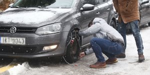 Άνδρας βάζει αλυσίδες στο αυτοκίνητό του σε ολισθηρό από το χιόνι δρόμο