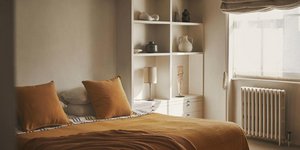 Κρεβατοκάμαρα διαμερίσματος με καφέ σεντόνια και μαξιλάρια, λευκή βιβλιοθήκη, διακοσμητικά, παράθυρο, καλοριφέρ