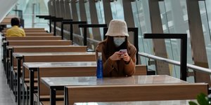 Γυναίκα με ιατρική μάσκα κοιτάζει το κινητό της σε τραπέζι