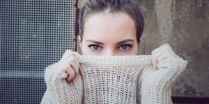 Γυναίκα κρύβει το πρόσωπό της με το πλεκτό και φαίνονται μόνο τα μάτια της