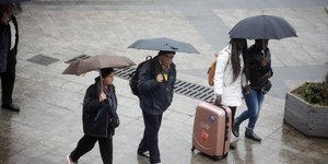 Κόσμος περπατά με ομπρέλες στη βροχή