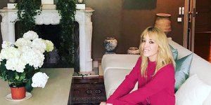 Η Νάντια Χαλαμανδάρη με φούξια κοστούμι κάθεται σε καναπέ