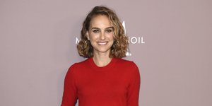 Η Νάταλι Πόρτμαν με κόκκινο τοπ και παντελόνι χαμογελά σε εκδήλωση