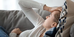 Γυναίκα ξαπλωμένη στον καναπέ με πονοκέφαλο