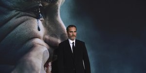Ο Joaquin Phoenix με κοστούμι μπροστά από αφίσα του Joker