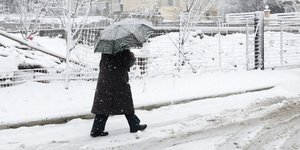 Άνδρας περπατά σε χιονισμένο δρόμο κρατώντας την ομπρέλα του