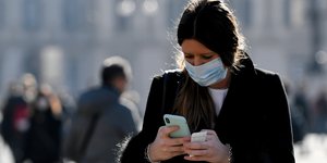 Γυναίκα με μάσκα στο Μιλάνο κοιτάζει το κινητό της