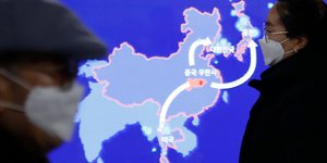 Άνθρωποι περνούν με μάσκες μπροστά από χάρτη της Κίνας